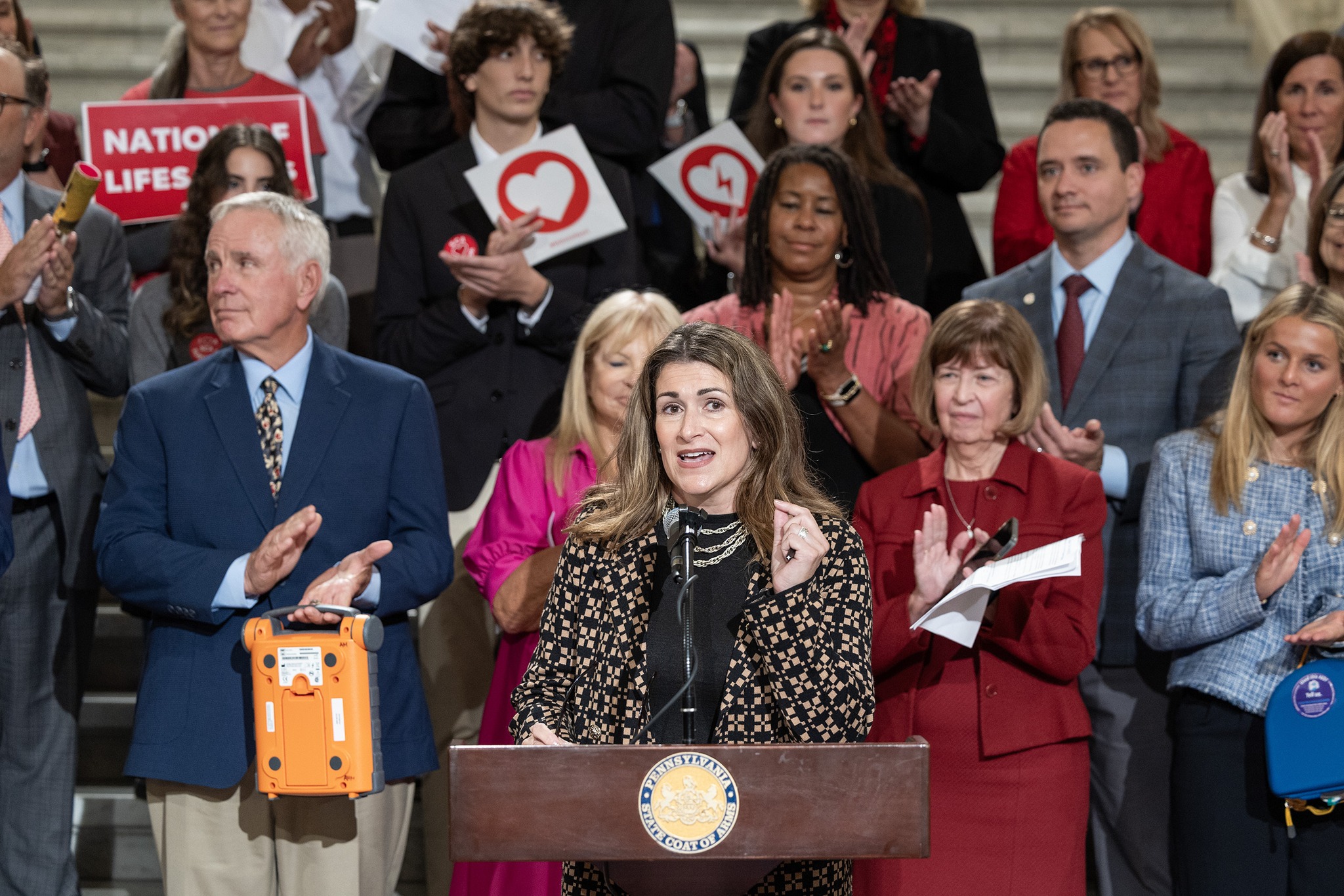 Sen. Rosemary Brown speaks in front of a crowd of dozens, speaking about her legislation: Greg Moyer’s Law. The crowd behind her is applauding the Senator, standing on the steps of the capitol rotunda.