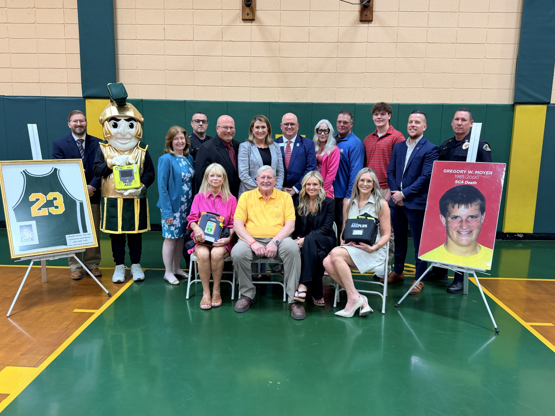 Sen. Brown poses for a photo with a group of people, including Greg Moyer’s family, partners, and advocates for this legislation in the gymnasium at Notre Dame Jr./Sr. High School.