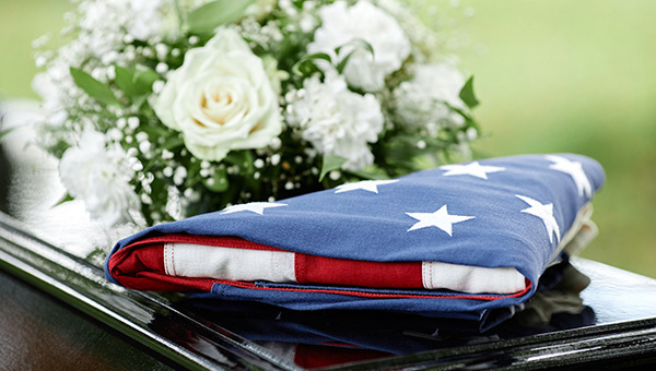 Closeup of folded American flag on coffin with flowers at outdoor funeral ceremony, copy space