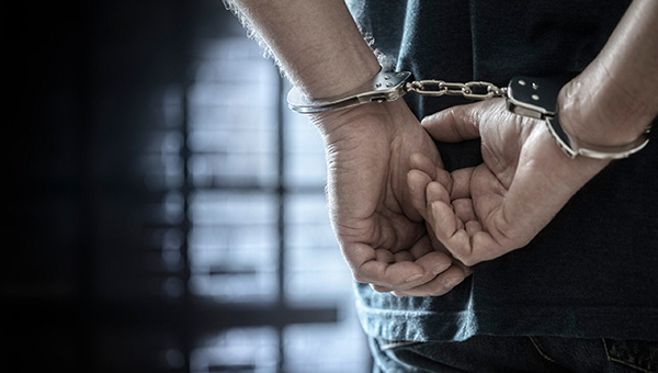 Arrested man in handcuffs with handcuffed hands behind back in prison