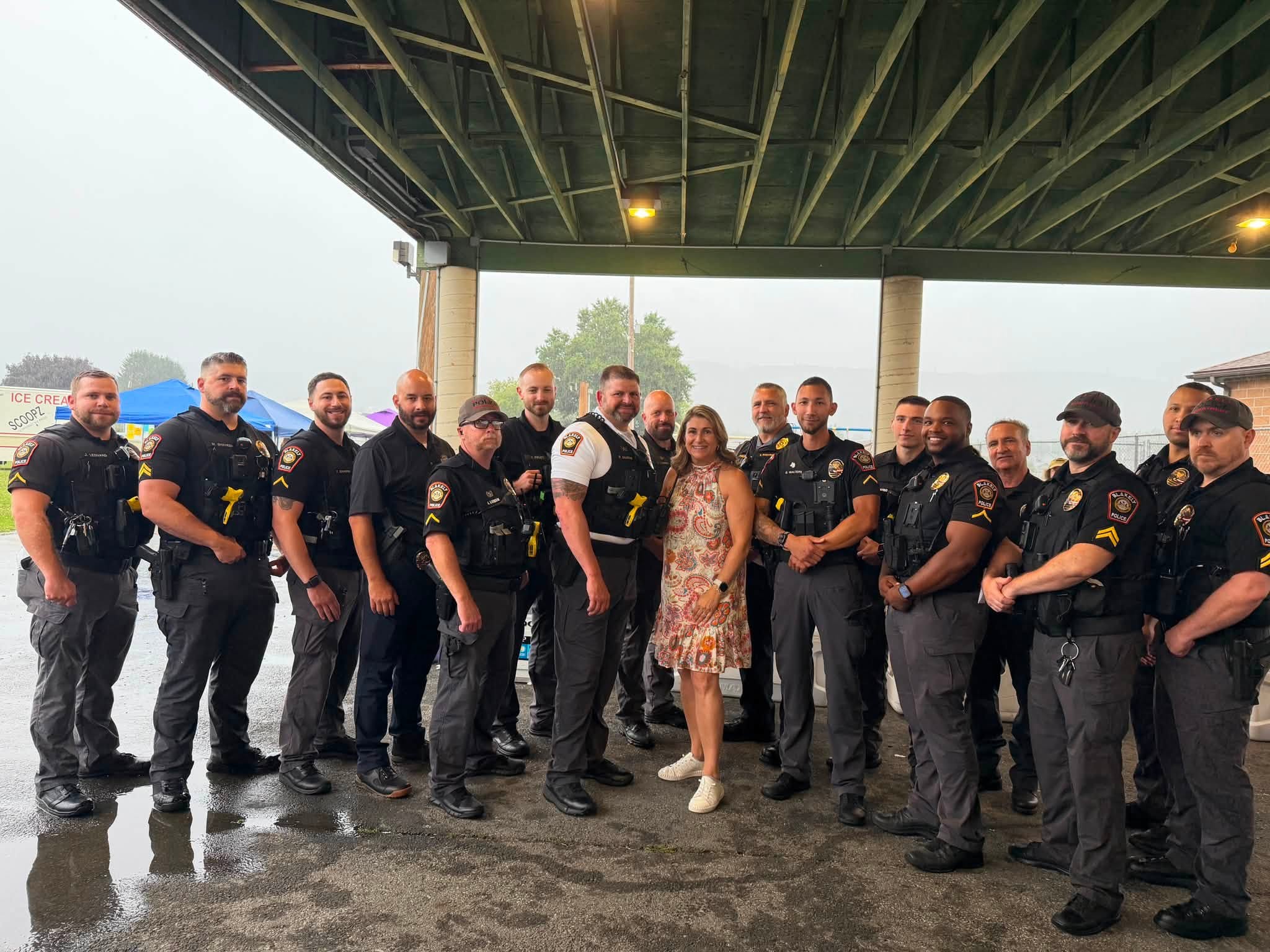 Sen. Rosemary Brown poses with a large group of police officers and community member at the Blakely Borough National Night Out event. They are under cover in a pavilion from the oncoming rain.